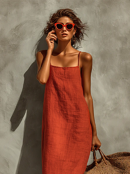 Red - Woman wearing a textured, relaxed-fit spaghetti strap maxi dress, holding a large woven tote bag against a concrete wall.