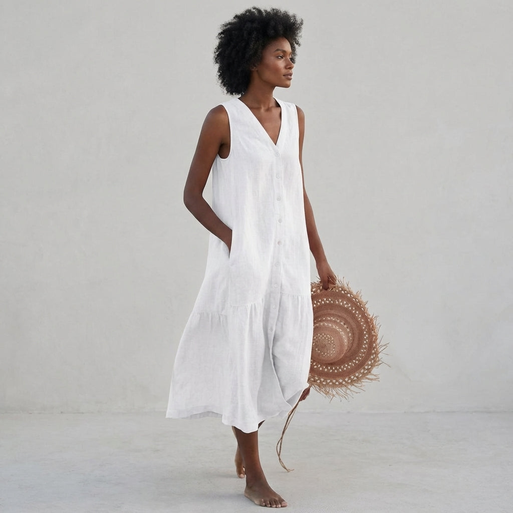 White - A woman wearing a sleeveless white linen midi dress with a V-neck, button-down front, and tiered skirt, holding a wide-brimmed straw hat against a neutral background.