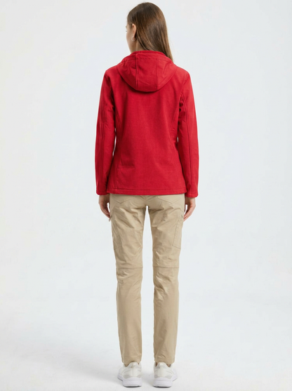 Red - A woman wearing a structured olive green matte technical hooded jacket with a front zip closure, panelled seam detailing, and zippered pockets, paired with beige trousers.