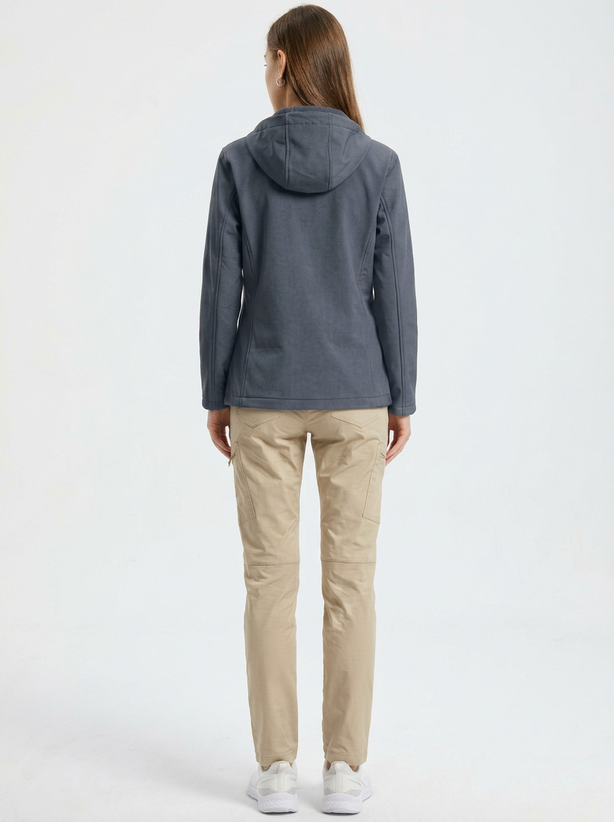 Gray - A woman wearing a structured olive green matte technical hooded jacket with a front zip closure, panelled seam detailing, and zippered pockets, paired with beige trousers.