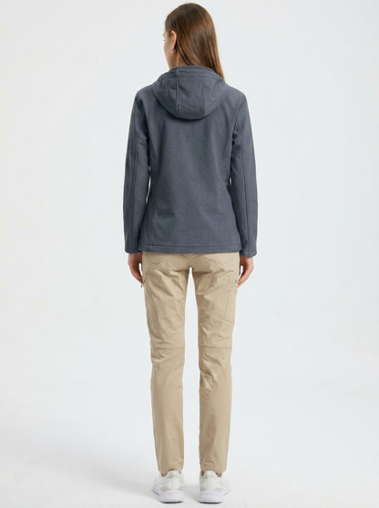 Gray - A woman wearing a structured olive green matte technical hooded jacket with a front zip closure, panelled seam detailing, and zippered pockets, paired with beige trousers.