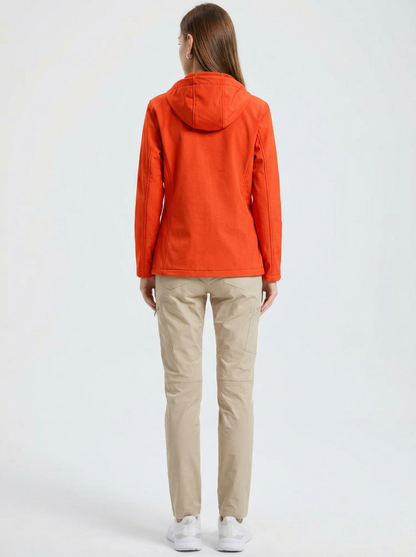 Orange - A woman wearing a structured olive green matte technical hooded jacket with a front zip closure, panelled seam detailing, and zippered pockets, paired with beige trousers.