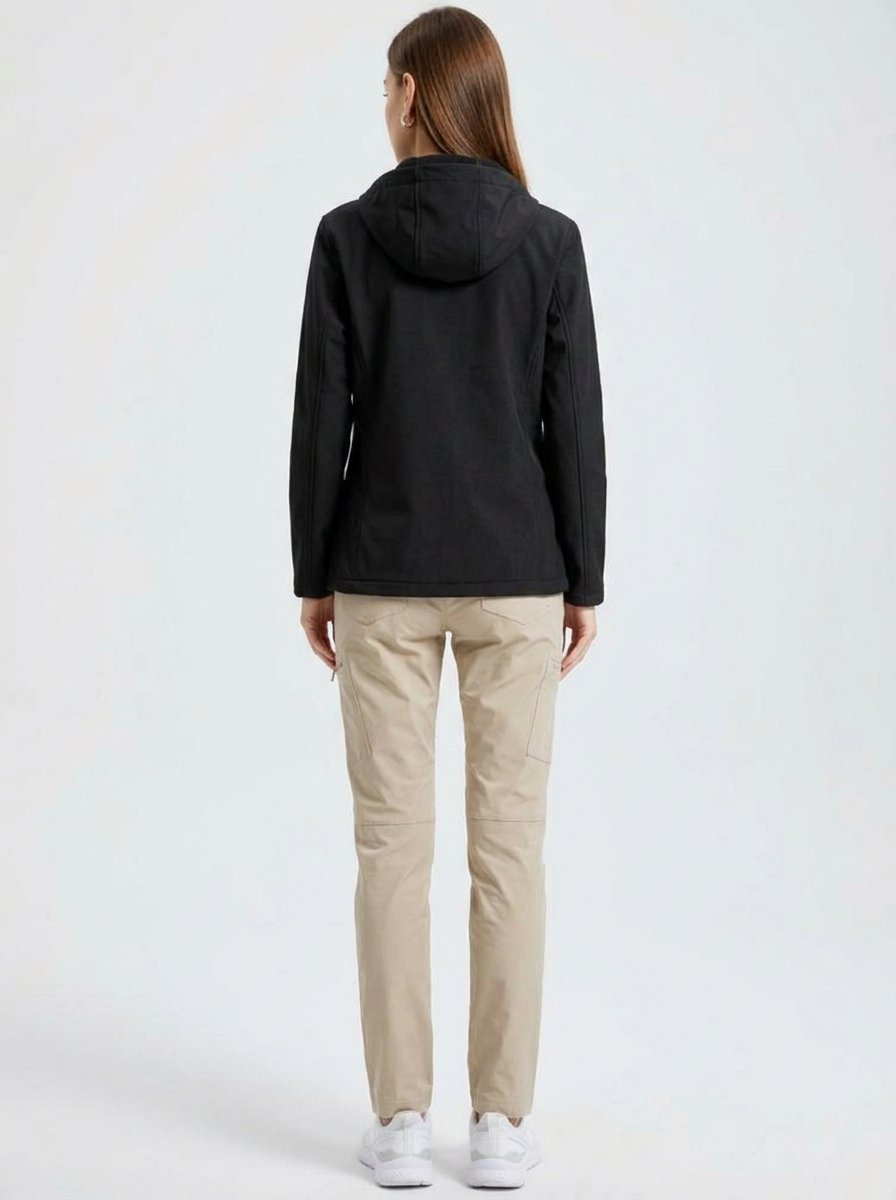 Black - A woman wearing a structured olive green matte technical hooded jacket with a front zip closure, panelled seam detailing, and zippered pockets, paired with beige trousers.