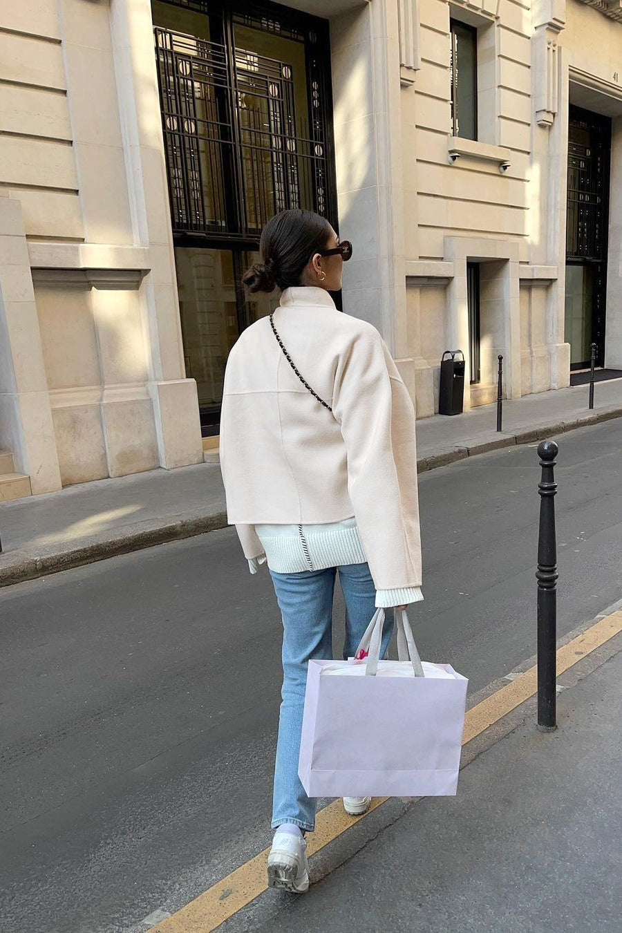Woman wearing an oversized, collarless, open-front cropped jacket in a light cream colour, styled over a white knit sweater and cream jeans.