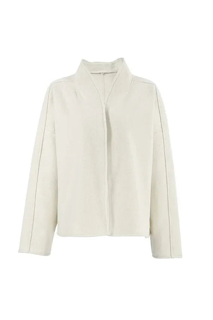 Apricot - Woman wearing an oversized, collarless, open-front cropped jacket in a light cream colour, styled over a white knit sweater and cream jeans.