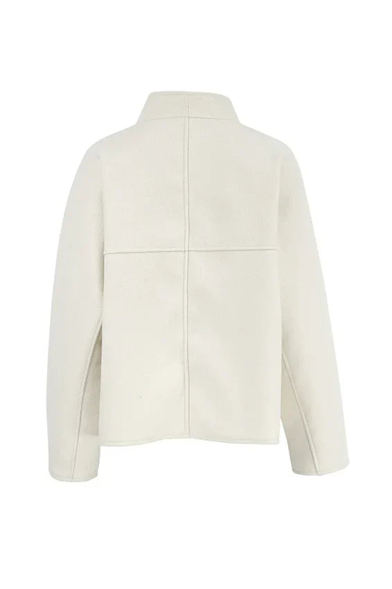Apricot - Woman wearing an oversized, collarless, open-front cropped jacket in a light cream colour, styled over a white knit sweater and cream jeans.