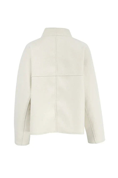 Apricot - Woman wearing an oversized, collarless, open-front cropped jacket in a light cream colour, styled over a white knit sweater and cream jeans.