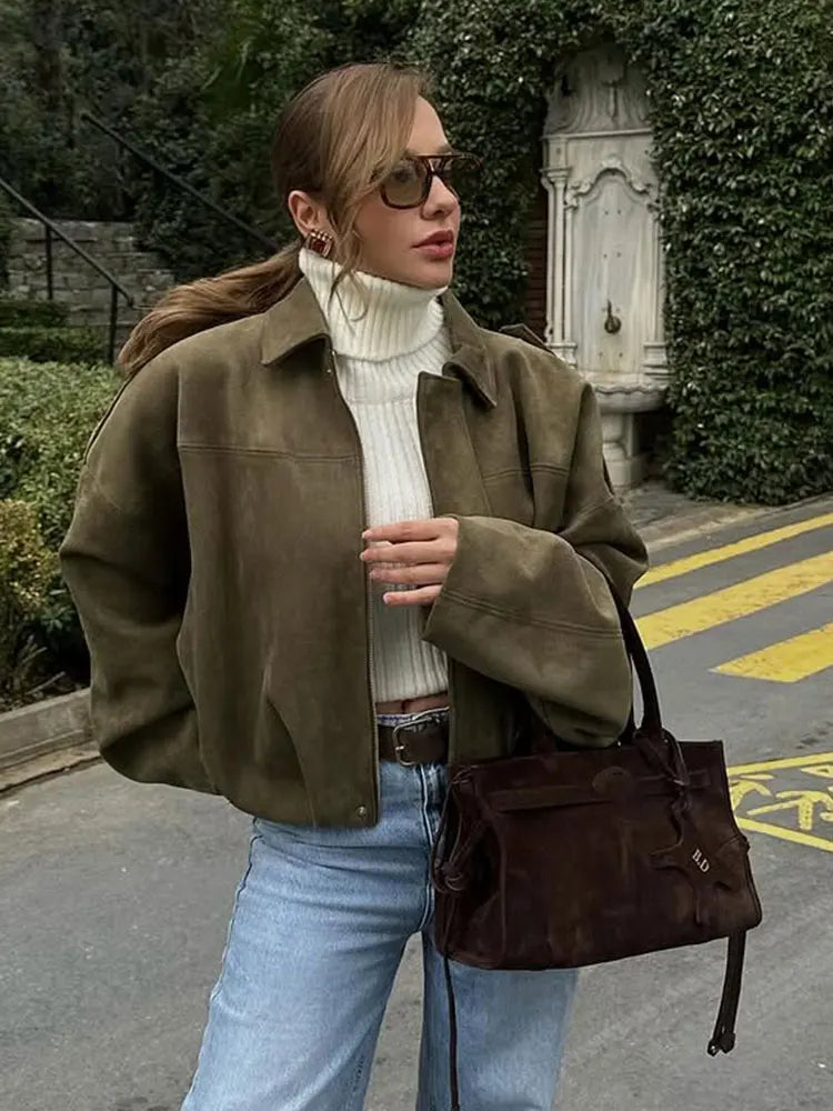 A woman taking a mirror selfie wearing an oversized, olive green faux-suede jacket with dropped shoulders, styled over a white top and dark grey jeans.