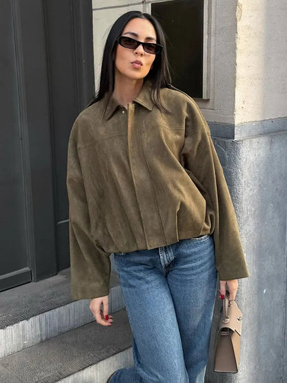 Green - A woman taking a mirror selfie wearing an oversized, olive green faux-suede jacket with dropped shoulders, styled over a white top and dark grey jeans.