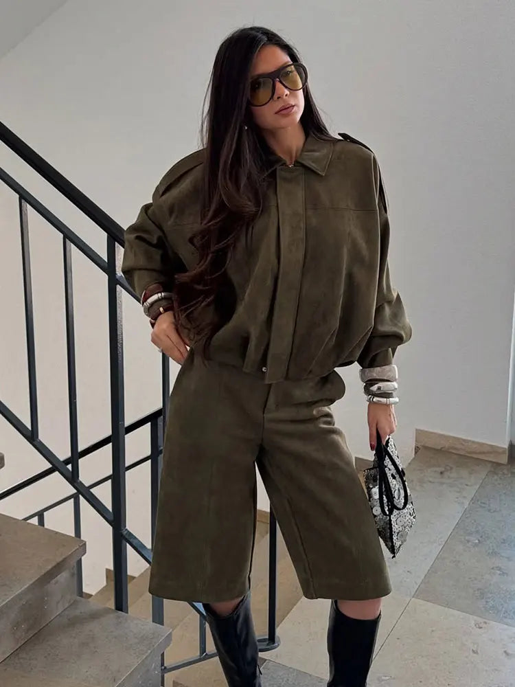 Green - A woman taking a mirror selfie wearing an oversized, olive green faux-suede jacket with dropped shoulders, styled over a white top and dark grey jeans.