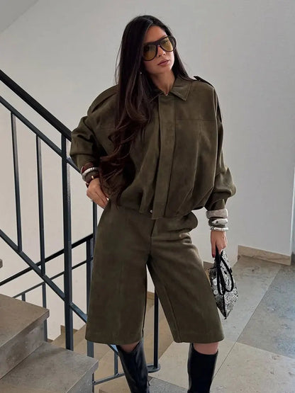Green - A woman taking a mirror selfie wearing an oversized, olive green faux-suede jacket with dropped shoulders, styled over a white top and dark grey jeans.