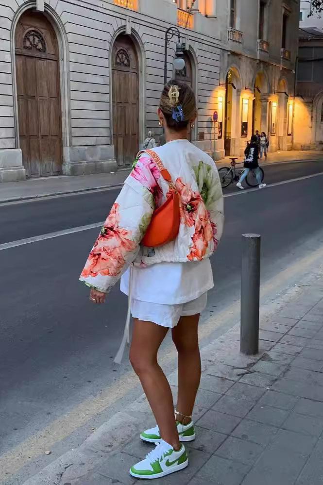 Women's oversized, cropped quilted jacket featuring a bold, large-scale floral print on a light background, styled with a snap-button front and drawstring hem.