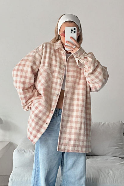 A woman taking a mirror selfie wearing an oversized, light pink and white plaid shacket over a white crop top and light wash denim jeans.