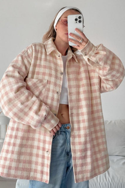 A woman taking a mirror selfie wearing an oversized, light pink and white plaid shacket over a white crop top and light wash denim jeans.
