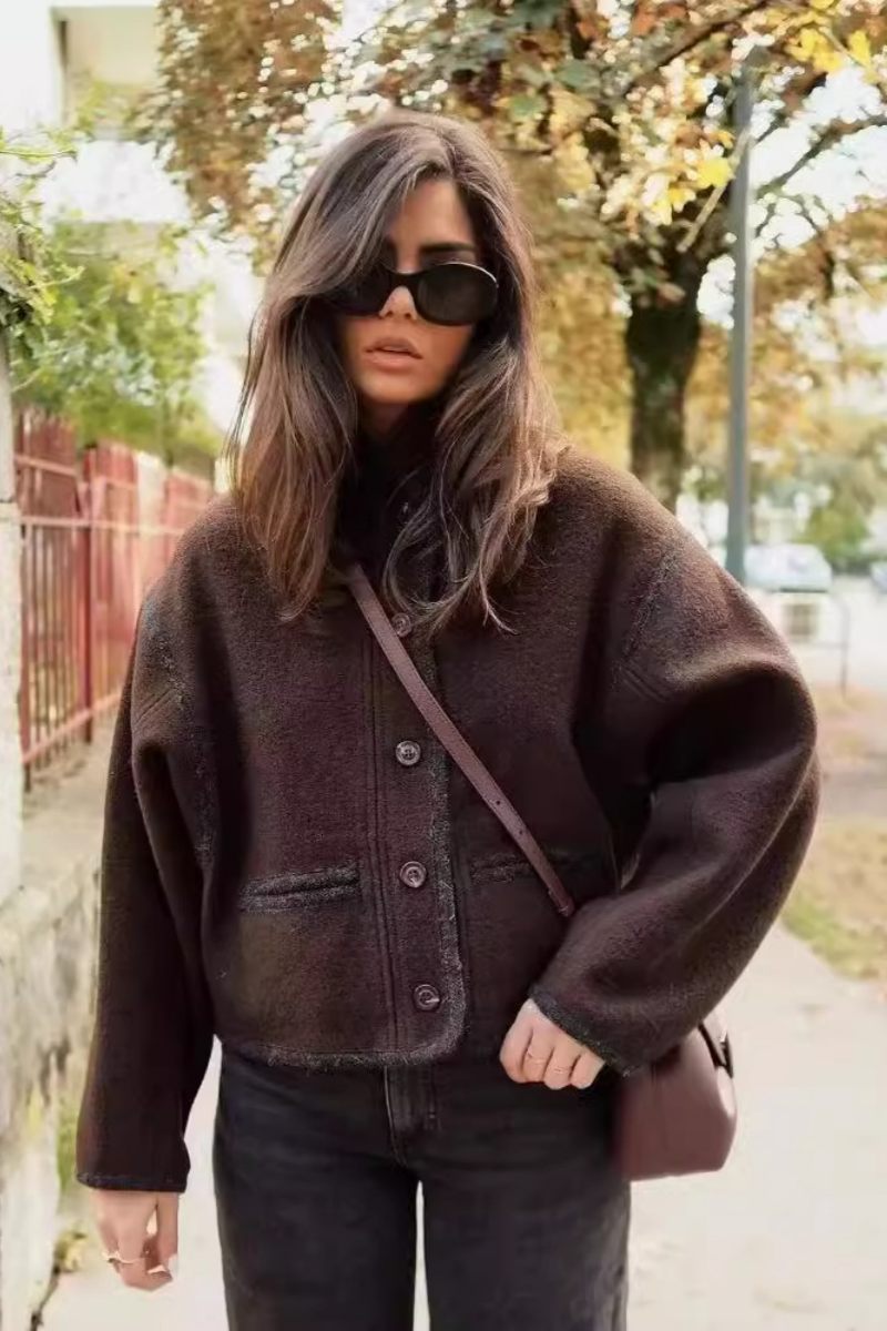 A woman wearing a dark brown, heavyweight textured cropped jacket with an oversized fit, button-front closure, and dropped shoulders, styled casually with dark denim.