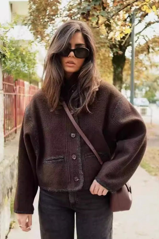 A woman wearing a dark brown, heavyweight textured cropped jacket with an oversized fit, button-front closure, and dropped shoulders, styled casually with dark denim.