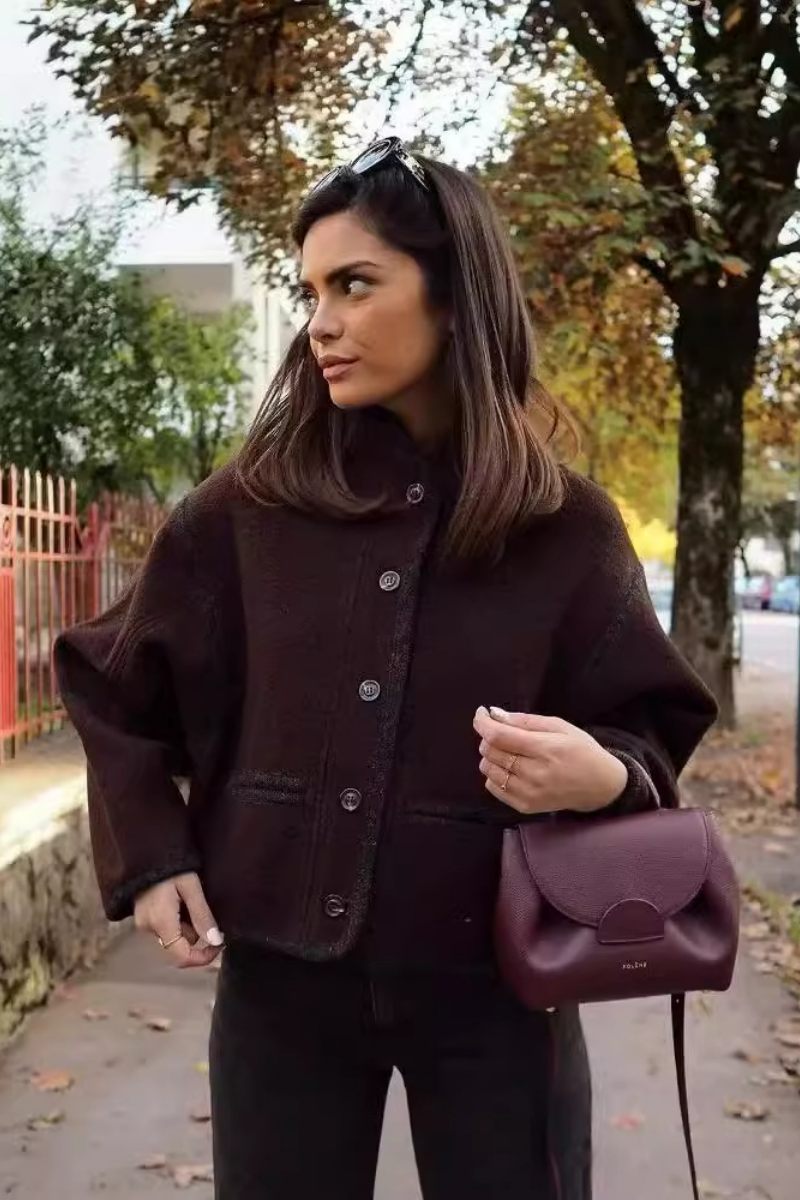 A woman wearing a dark brown, heavyweight textured cropped jacket with an oversized fit, button-front closure, and dropped shoulders, styled casually with dark denim.