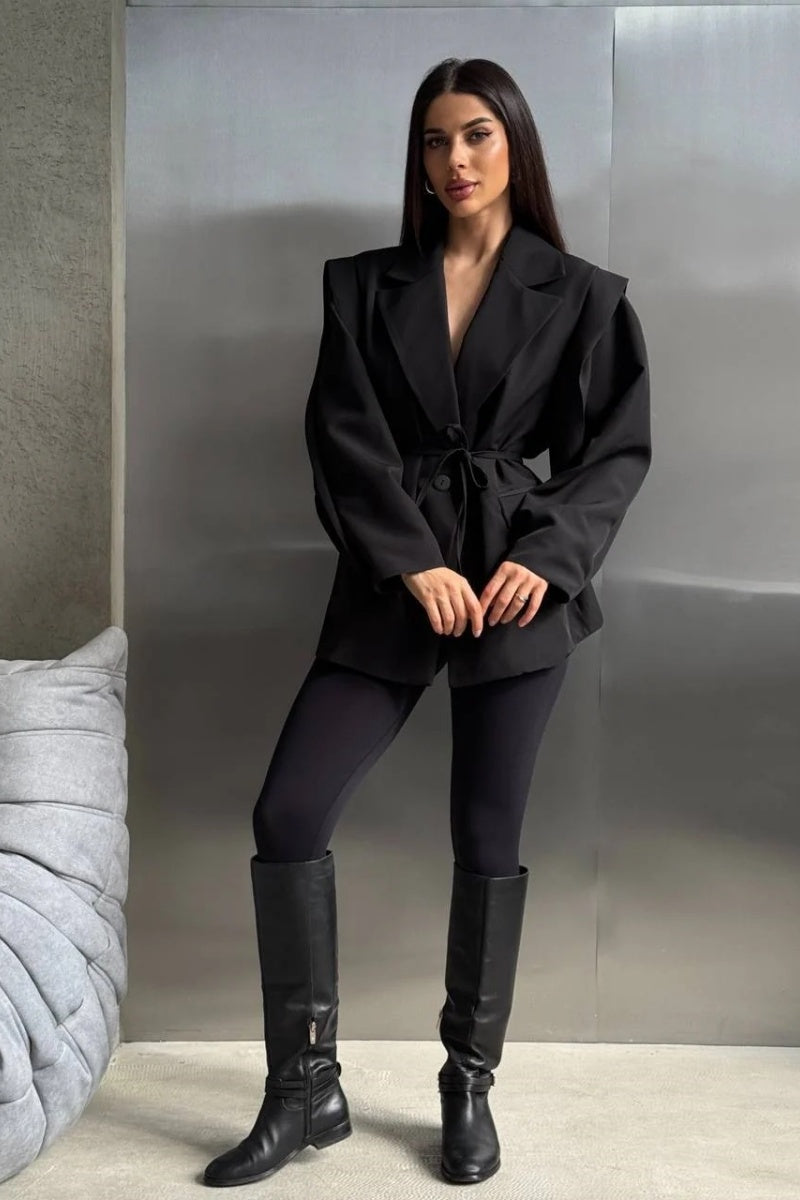 Black - Woman wearing a black oversized blazer with structured shoulders and a tie waist, paired with black leggings and knee-high boots.