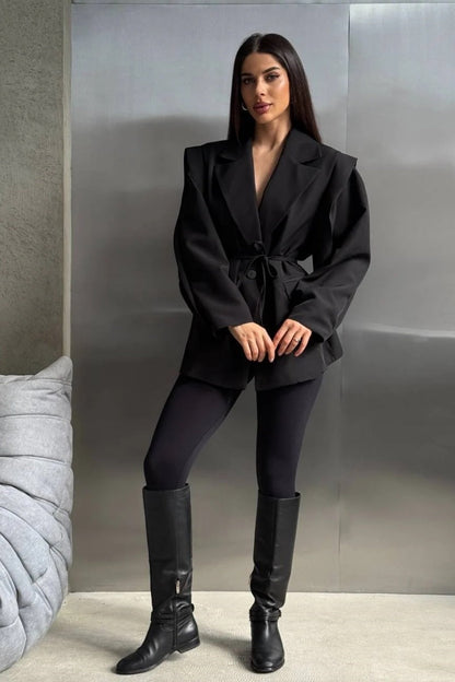 Black - Woman wearing a black oversized blazer with structured shoulders and a tie waist, paired with black leggings and knee-high boots.