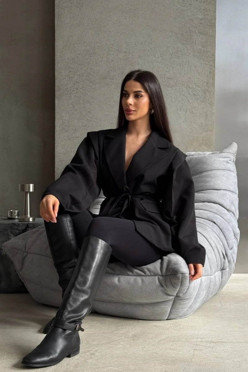 Black - Woman wearing a black oversized blazer with structured shoulders and a tie waist, paired with black leggings and knee-high boots.