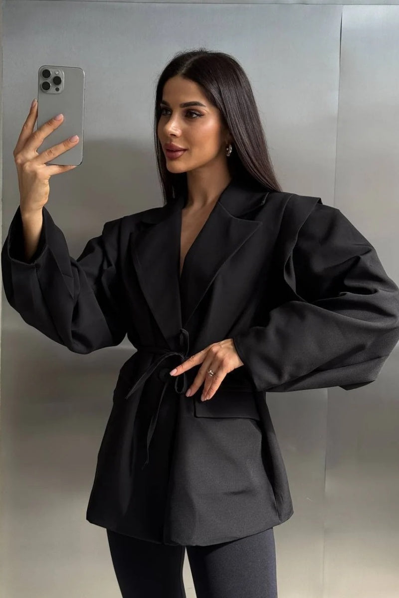 Black - Woman wearing a black oversized blazer with structured shoulders and a tie waist, paired with black leggings and knee-high boots.