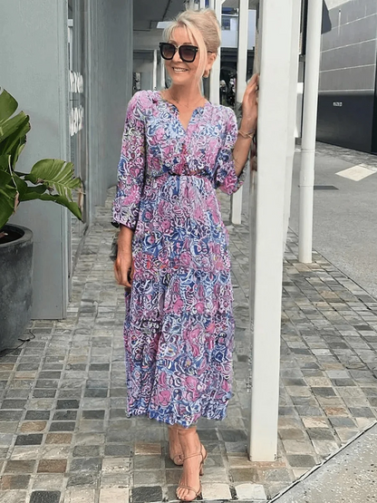 Pink - Woman wearing a flowing paisley print maxi dress with 3/4 sleeves, a tie waist, and a tiered skirt.