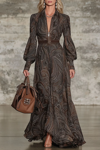 Brown - A model wears a long-sleeved, floor-length maxi dress featuring an intricate brown and tan paisley print, a zip-front collared neckline, and voluminous blouson sleeves.