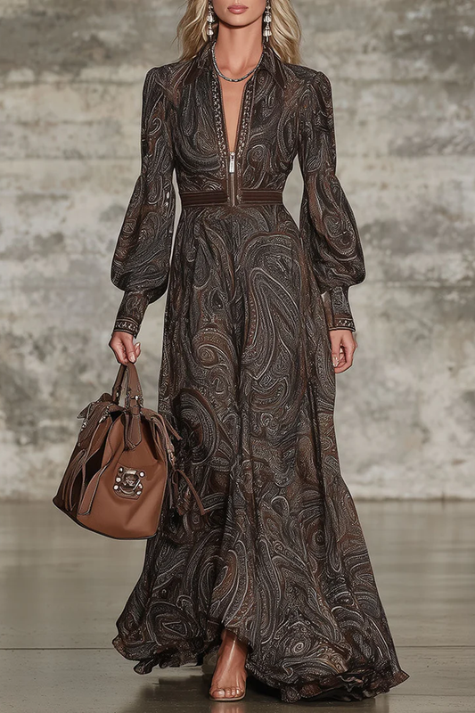 Brown - A model wears a long-sleeved, floor-length maxi dress featuring an intricate brown and tan paisley print, a zip-front collared neckline, and voluminous blouson sleeves.