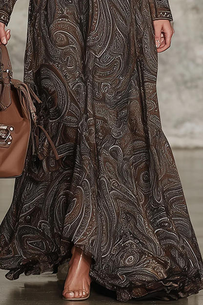 Brown - A model wears a long-sleeved, floor-length maxi dress featuring an intricate brown and tan paisley print, a zip-front collared neckline, and voluminous blouson sleeves.