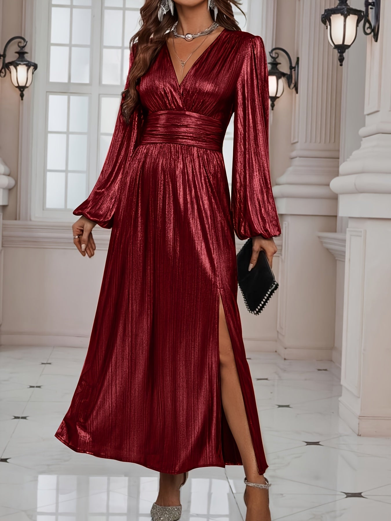 Woman wearing a shiny metallic pleated long sleeve maxi dress with a wrap bodice, banded waist, and high leg slit, standing in a formal indoor setting.