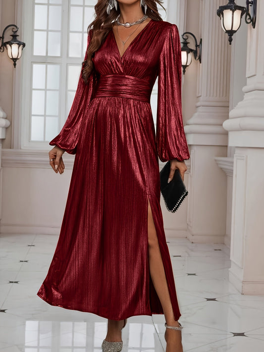 Woman wearing a shiny metallic pleated long sleeve maxi dress with a wrap bodice, banded waist, and high leg slit, standing in a formal indoor setting.