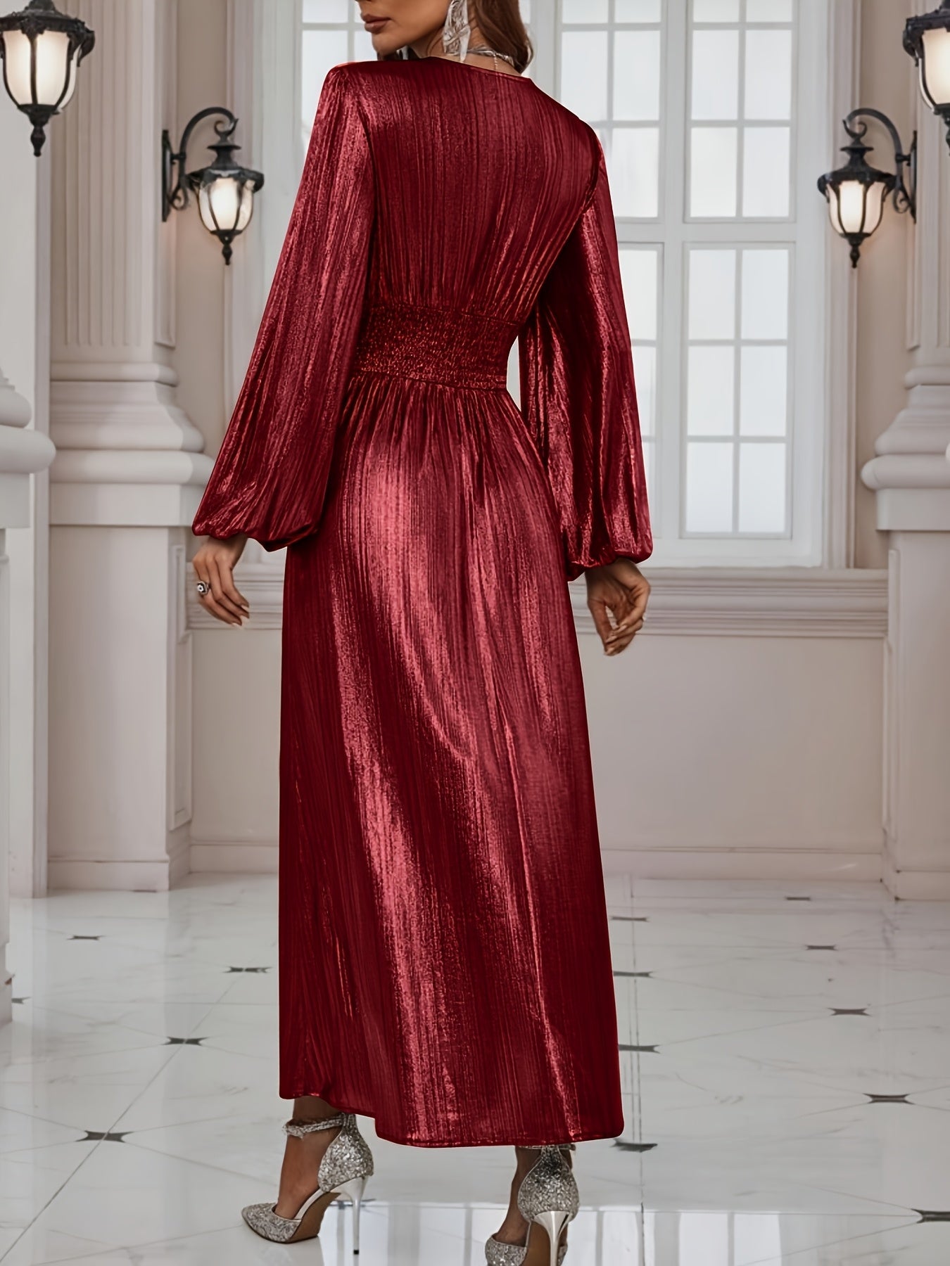 Woman wearing a shiny metallic pleated long sleeve maxi dress with a wrap bodice, banded waist, and high leg slit, standing in a formal indoor setting.