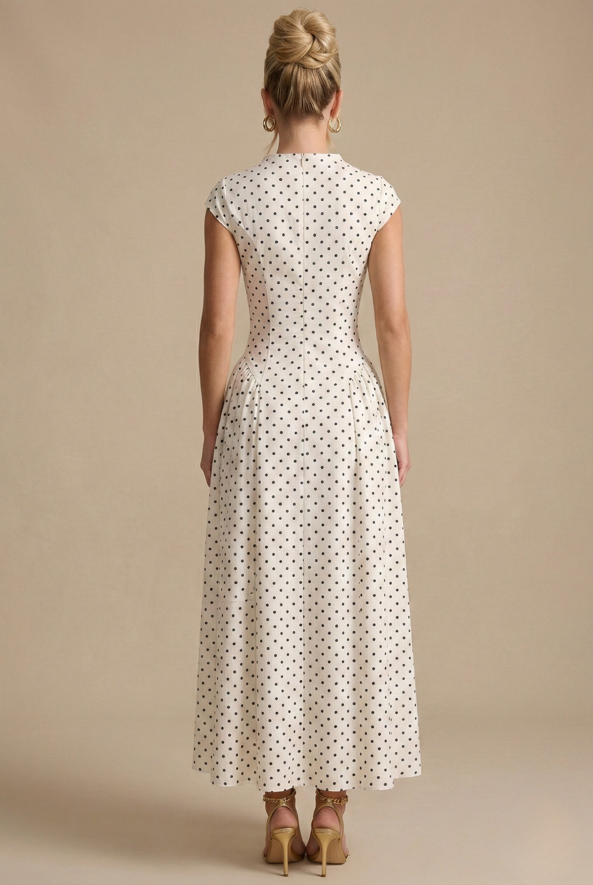 White - Model wearing a white and black polka dot maxi dress featuring a high neckline, cap sleeves, a fitted bodice with a basque waist, and a full pleated A-line skirt.