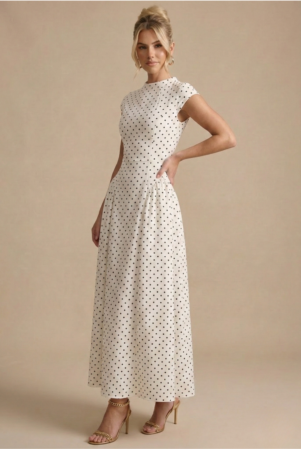 White - Model wearing a white and black polka dot maxi dress featuring a high neckline, cap sleeves, a fitted bodice with a basque waist, and a full pleated A-line skirt.