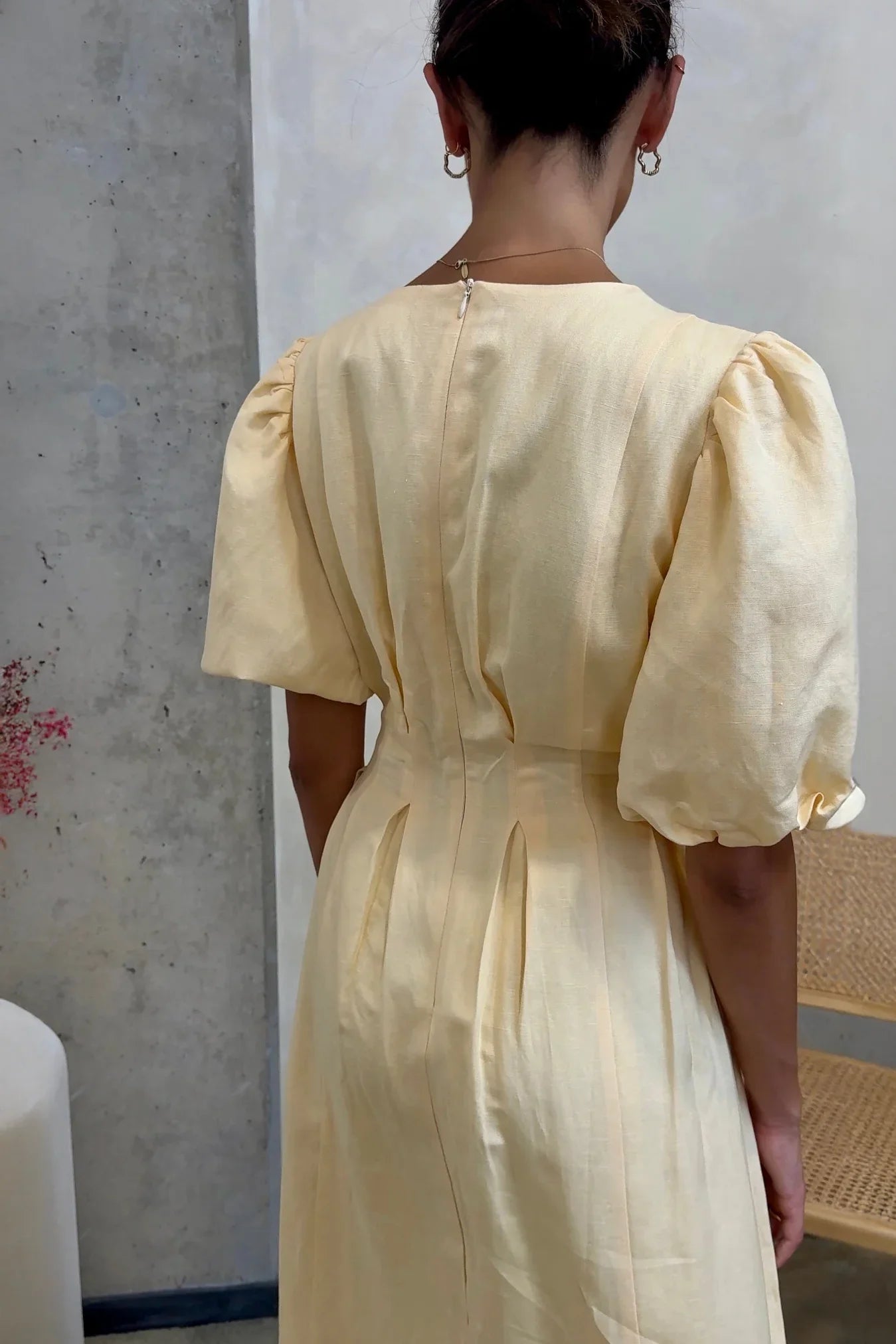 Butter Yellow - A woman wearing a pale yellow midi dress with short puff sleeves, a fitted waist, and a pleated skirt, standing in a minimalist studio setting.