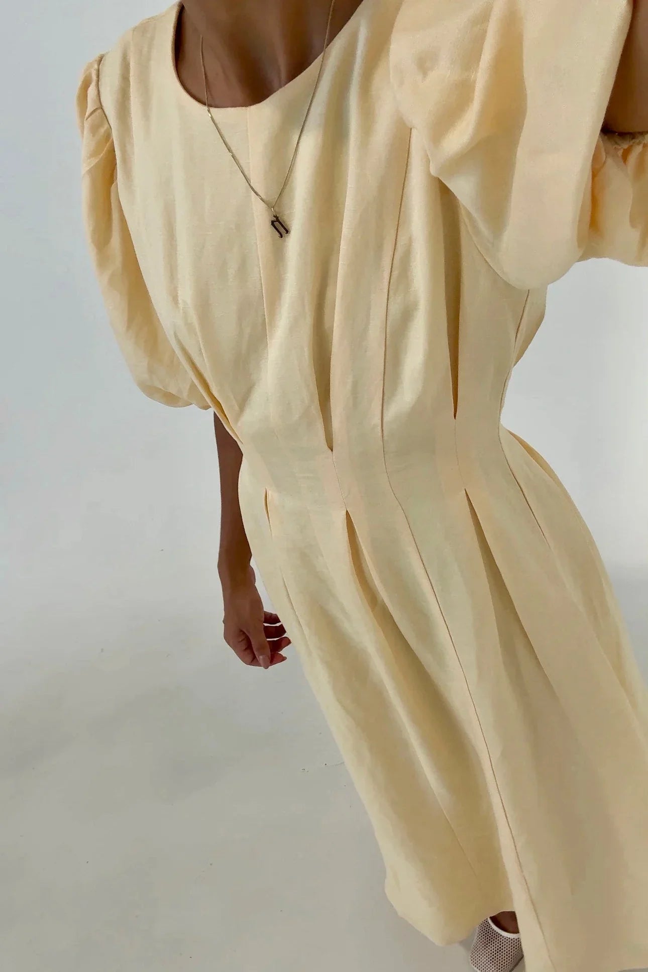 Butter Yellow - A woman wearing a pale yellow midi dress with short puff sleeves, a fitted waist, and a pleated skirt, standing in a minimalist studio setting.
