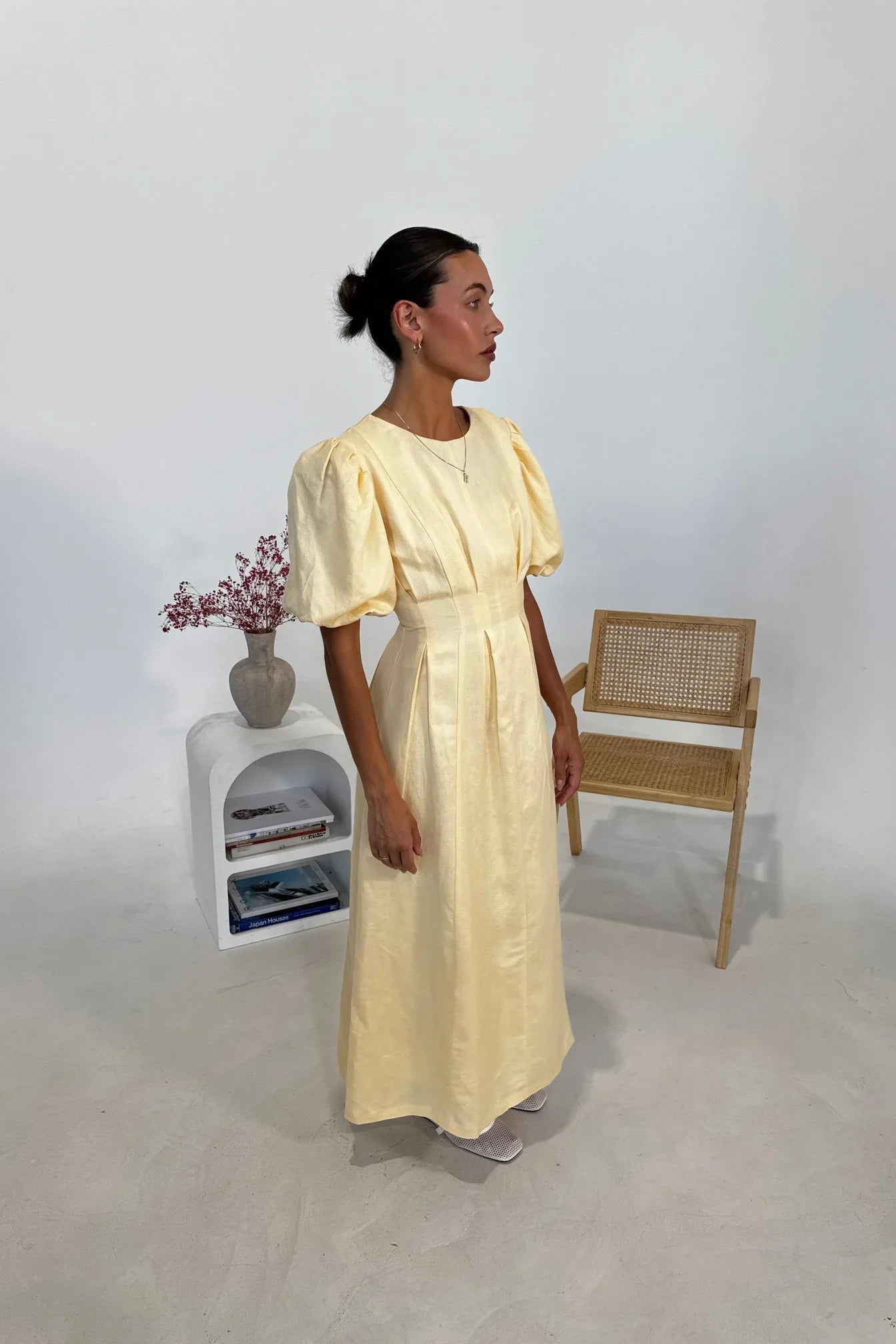 Butter Yellow - A woman wearing a pale yellow midi dress with short puff sleeves, a fitted waist, and a pleated skirt, standing in a minimalist studio setting.