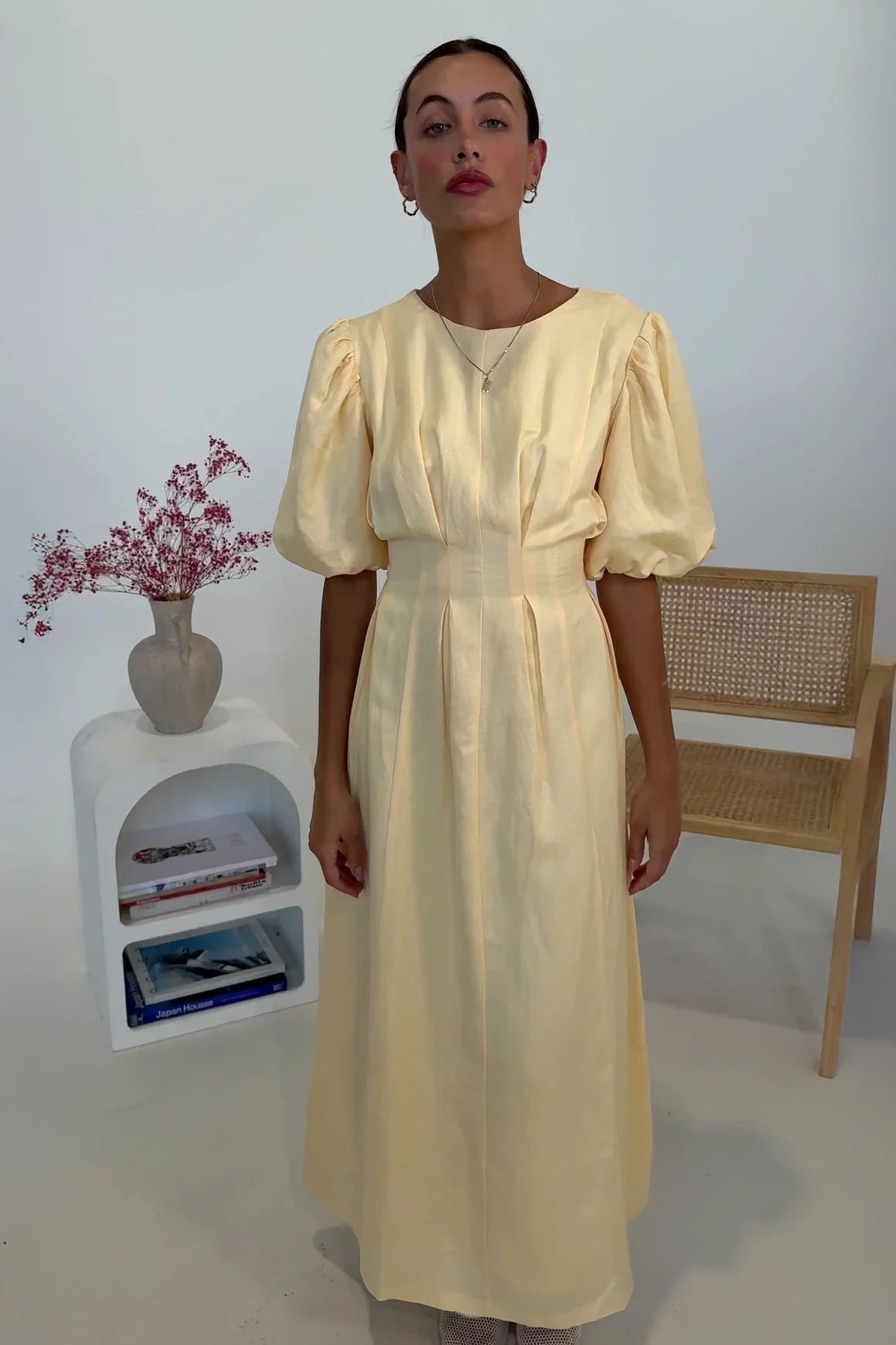 Butter Yellow - A woman wearing a pale yellow midi dress with short puff sleeves, a fitted waist, and a pleated skirt, standing in a minimalist studio setting.