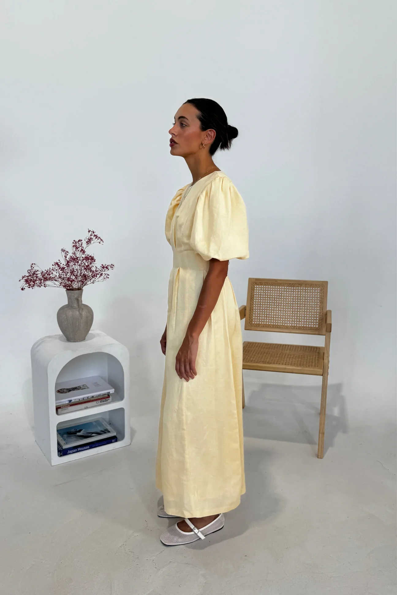 Butter Yellow - A woman wearing a pale yellow midi dress with short puff sleeves, a fitted waist, and a pleated skirt, standing in a minimalist studio setting.