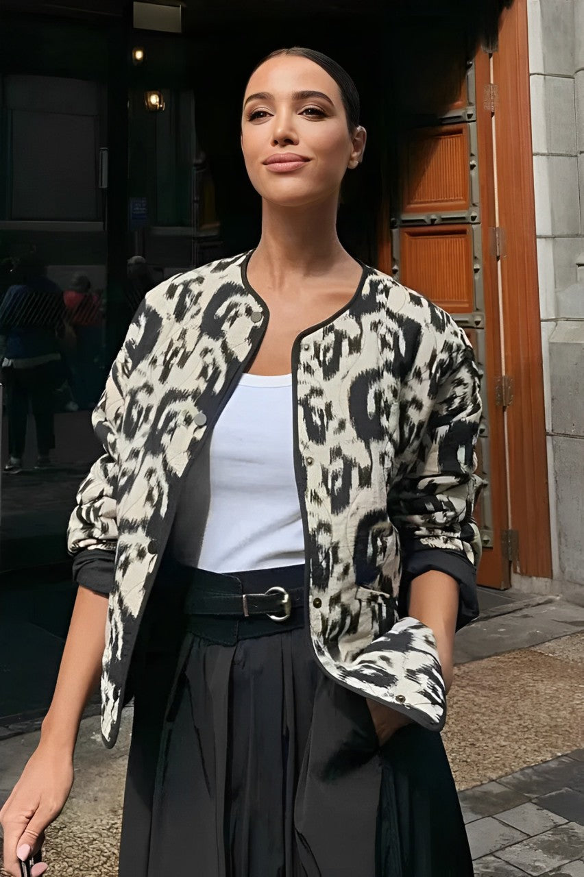 Woman wearing a smart casual quilted collarless jacket with an abstract black and white print, layered over a white top and black bottoms.