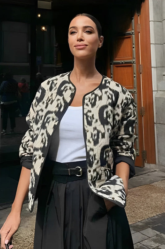 Woman wearing a smart casual quilted collarless jacket with an abstract black and white print, layered over a white top and black bottoms.