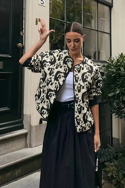Woman wearing a smart casual quilted collarless jacket with an abstract black and white print, layered over a white top and black bottoms.