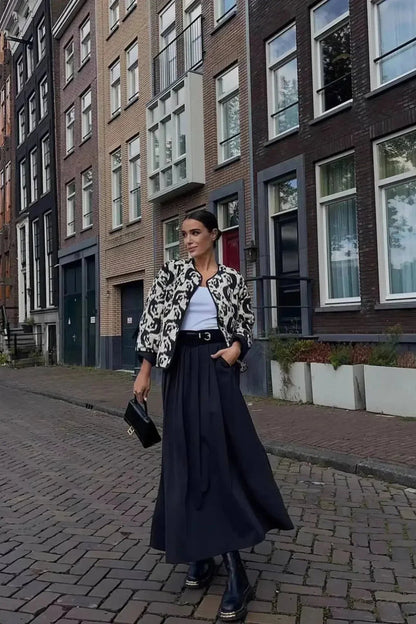 Woman wearing a smart casual quilted collarless jacket with an abstract black and white print, layered over a white top and black bottoms.