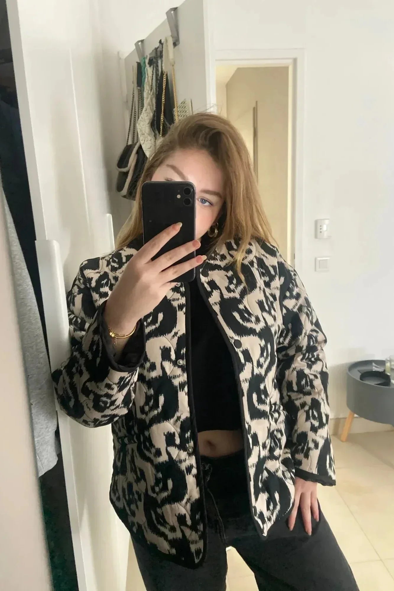 Woman wearing a smart casual quilted collarless jacket with an abstract black and white print, layered over a white top and black bottoms.