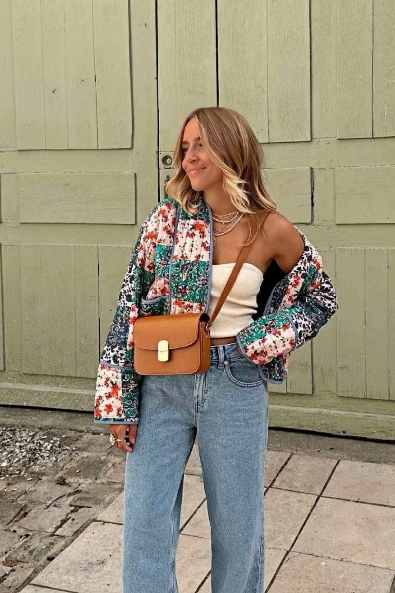 Woman wearing a quilted patchwork jacket with floral prints over a white tube top and blue jeans, standing outdoors.
