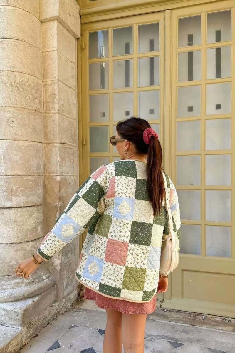 A woman wearing a quilted patchwork jacket with floral and solid panels, styled over a beige shirt and pink textured mini skirt.