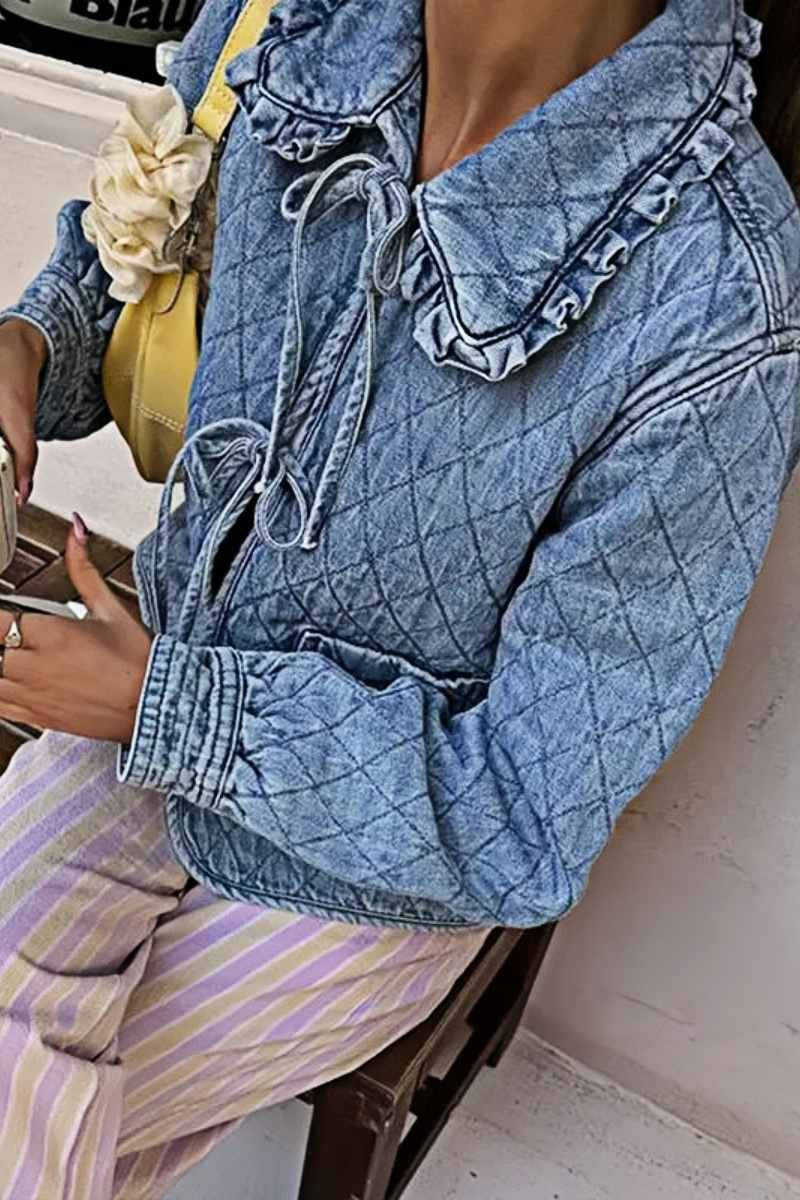 Women's blue diamond-quilted denim jacket featuring a ruffled collar, tie-front closure, and voluminous balloon sleeves, styled with distressed shorts and cowboy boots.