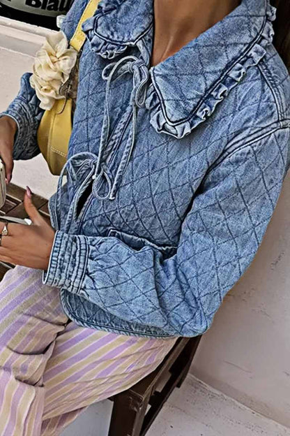 Women's blue diamond-quilted denim jacket featuring a ruffled collar, tie-front closure, and voluminous balloon sleeves, styled with distressed shorts and cowboy boots.