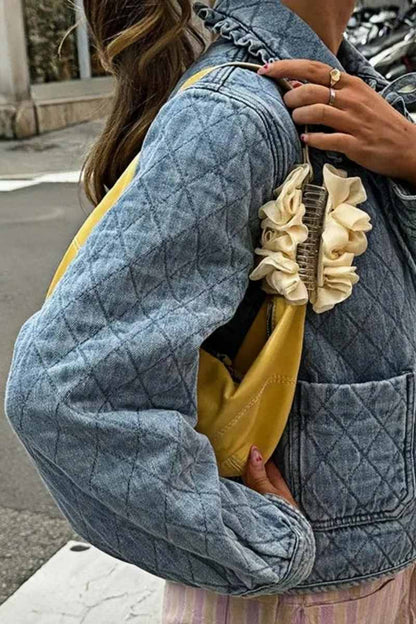 Women's blue diamond-quilted denim jacket featuring a ruffled collar, tie-front closure, and voluminous balloon sleeves, styled with distressed shorts and cowboy boots.