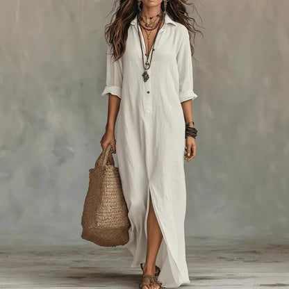 White - A woman wearing a relaxed-fit white linen maxi sundress with a pointed collar, button placket, and front slit, carrying a woven straw bag.